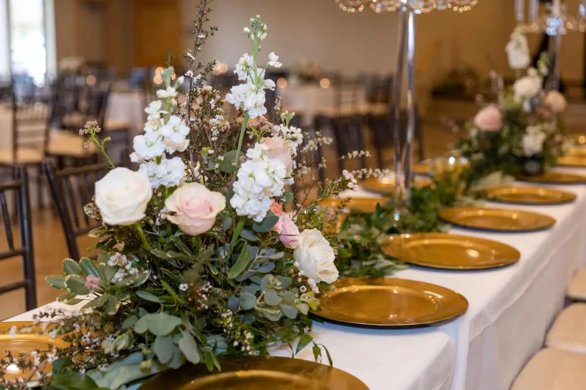 The head table with gold chargers and a low floral runner