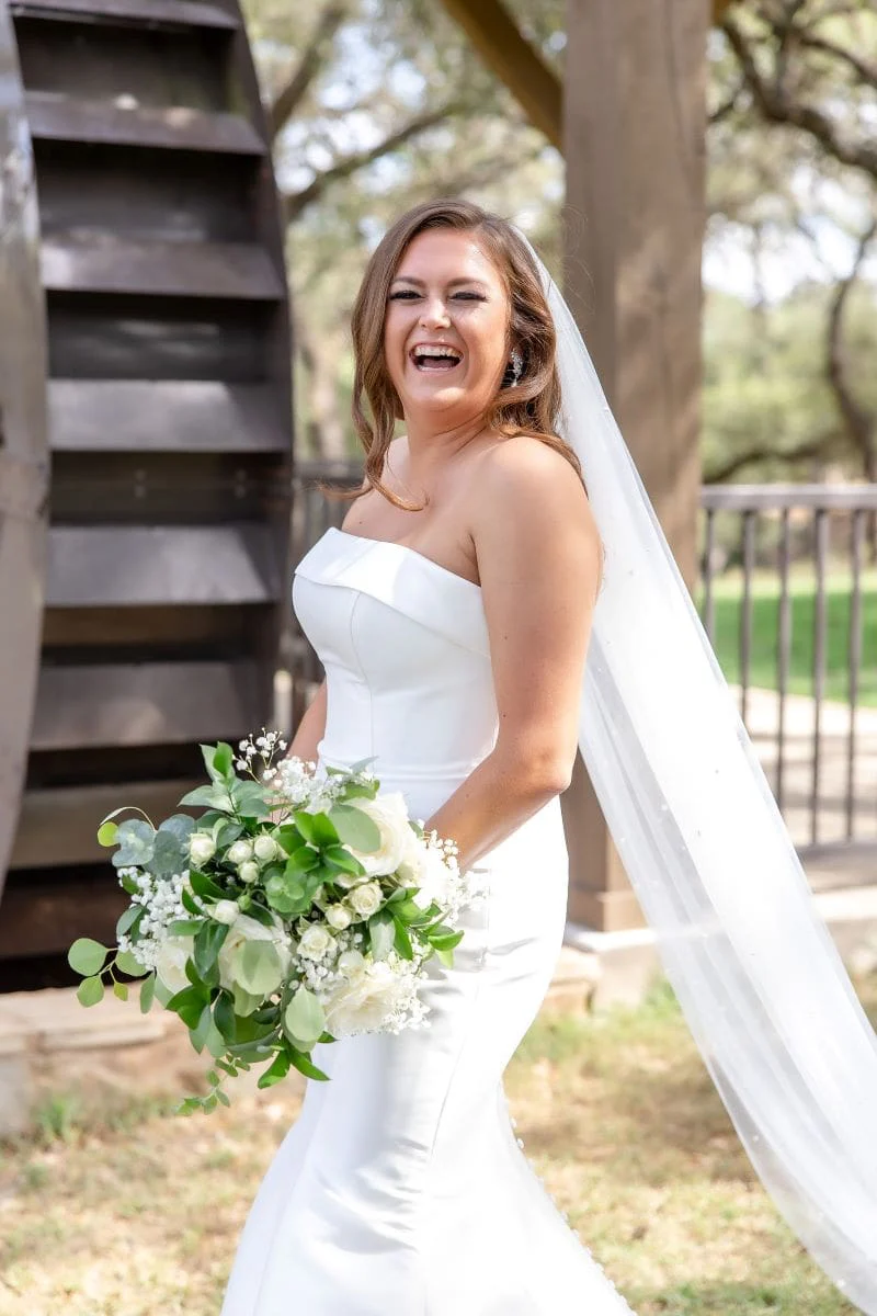Meghan laughing with her greenery bouquet, veil trailing behind her