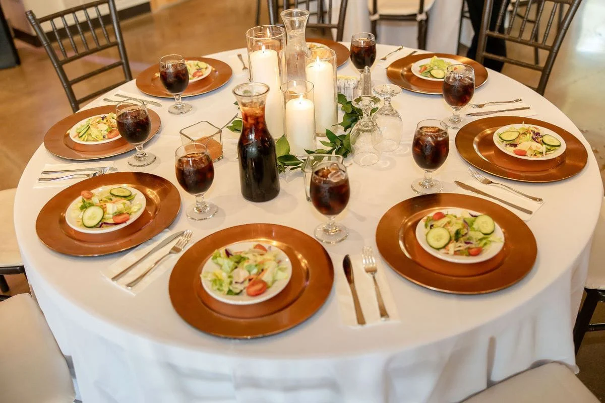 A guest table with copper chargers, salads and pillar candles