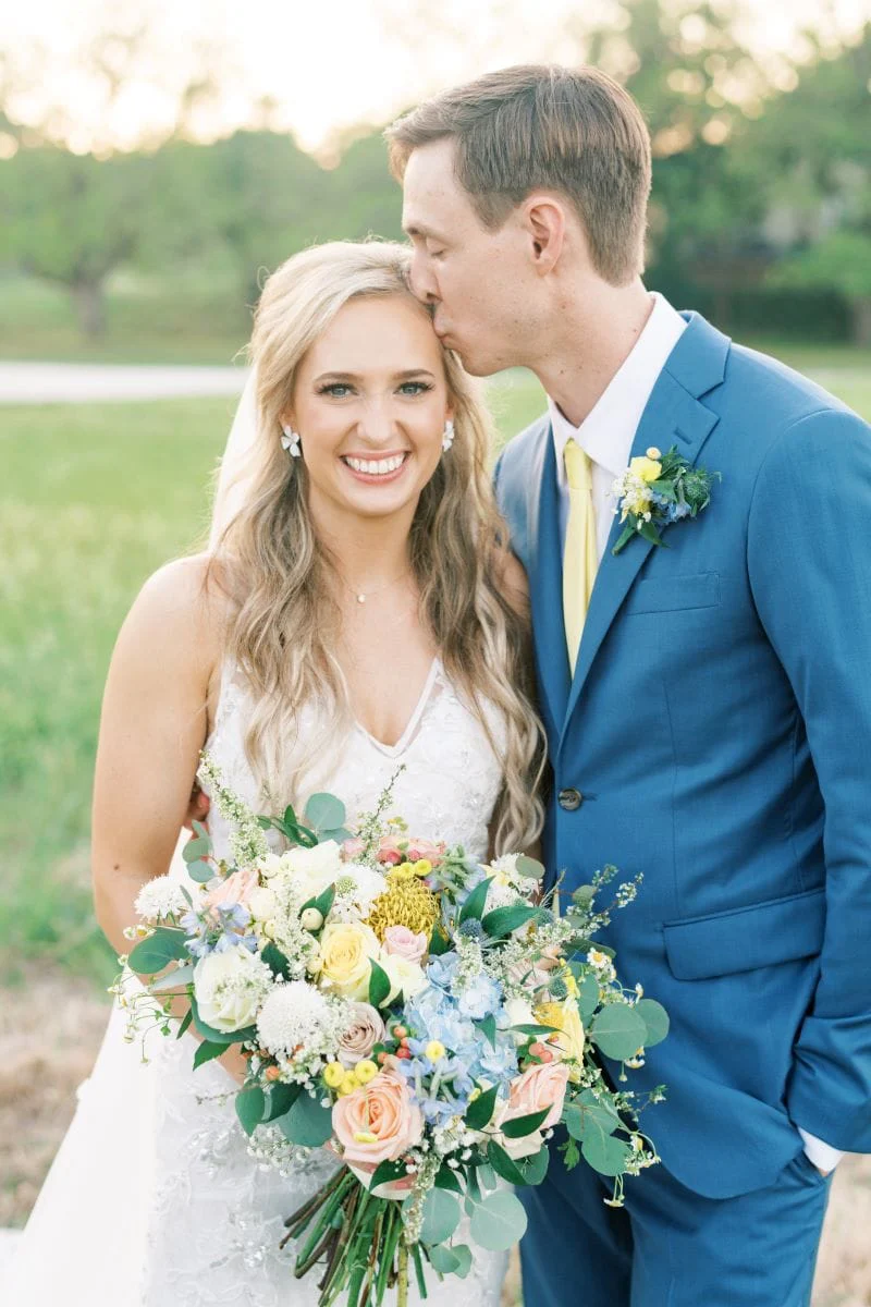 Jackson kissing Sara Kathryn’s temple, her pastel bouquet in hand