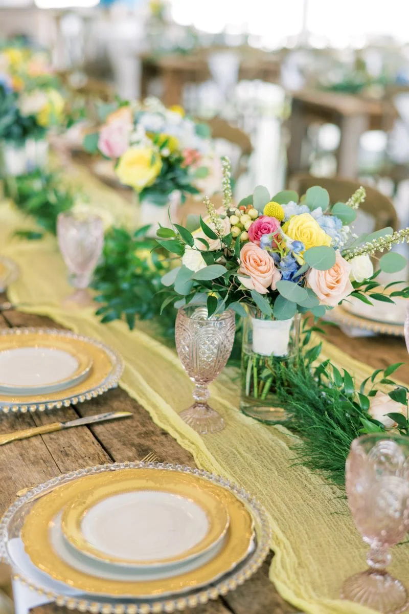 The head table under a yellow gauze runner and gold rimmed china
