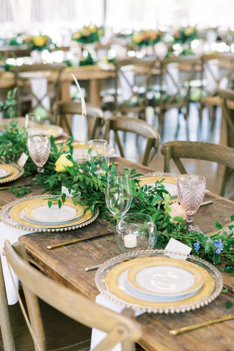 A reception table with gold chargers, greenery and pink goblets