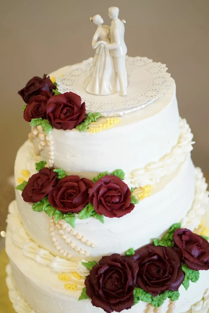 The three-tier cake her cousin made, trimmed with burgundy roses