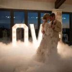 Smoke machine and letter lighting behind a bride and groom dancing