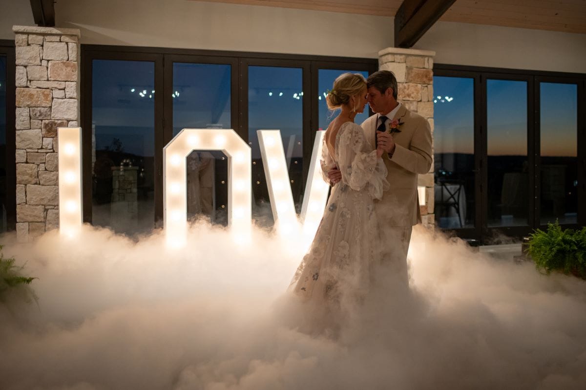 Smoke machine and letter lighting behind a bride and groom dancing