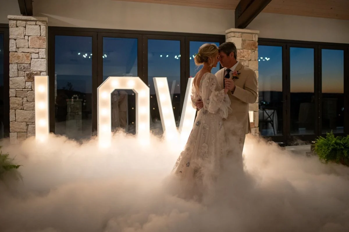 Smoke machine and letter lighting behind a bride and groom dancing
