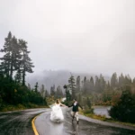 A couple on their wedding day walking on a rain-soaked road, captured by MobilBoheme photographers and wedding videographers