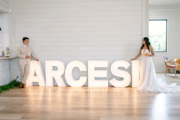 A couple standing either side of large lit marquee letters in a white event hall