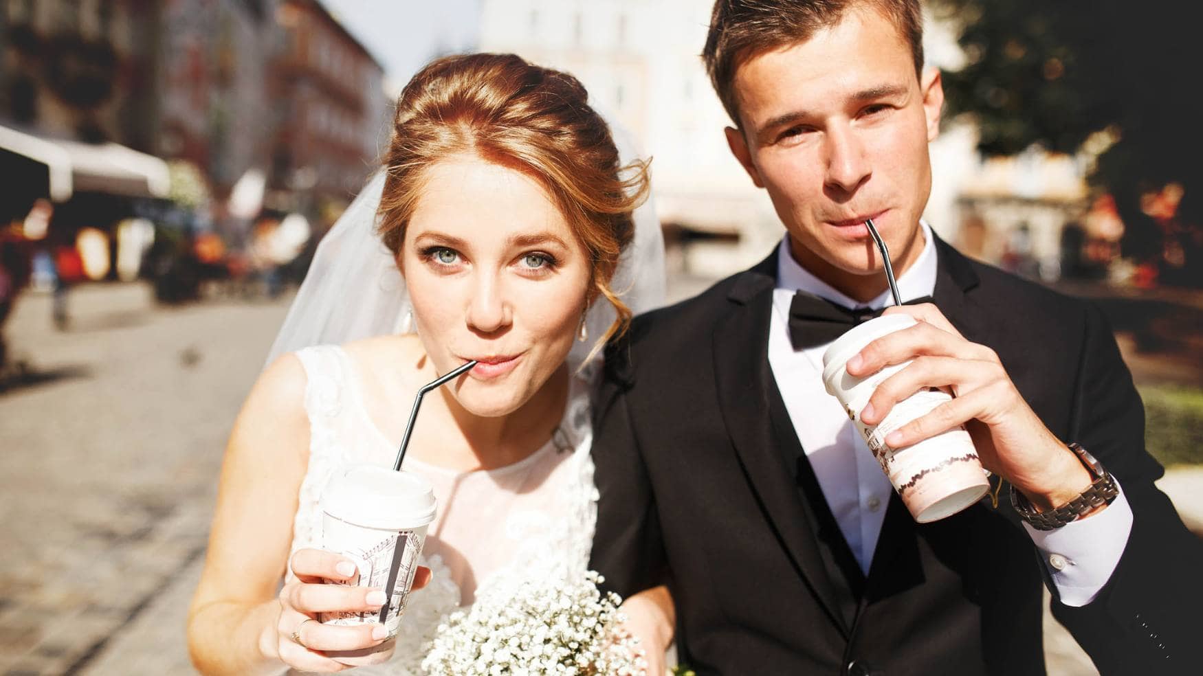 A bride and groom drinking coffee while walking on the street