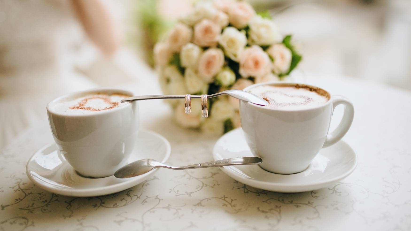 Two ceramic coffee cups with coffee next to a bridal flower bouquet