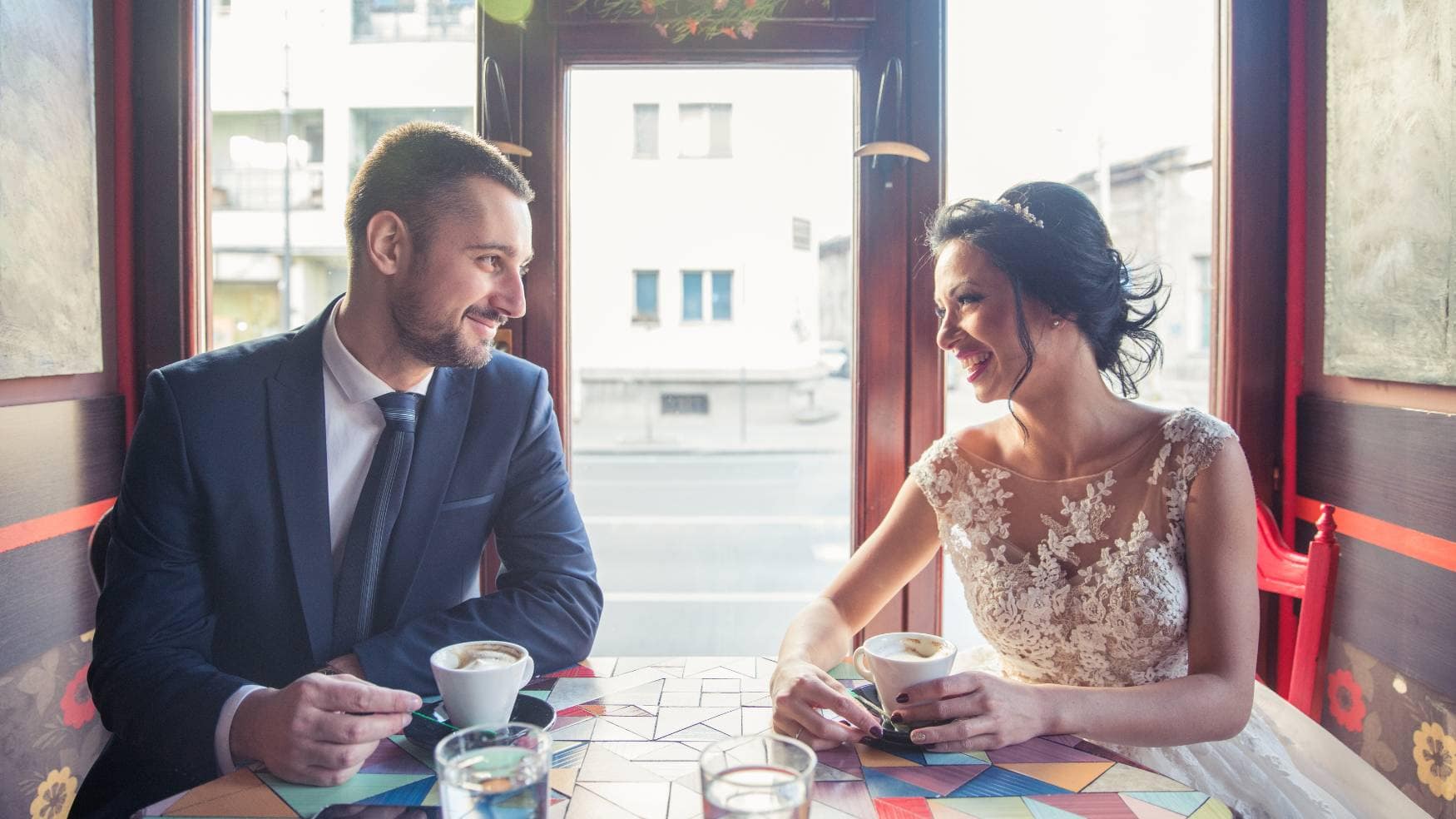 A bride and groom posing at a table drinking coffee from their wedding coffee bar