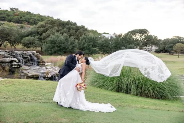 A couple kissing on a lawn beside a waterfall, the bride's veil sweeping wide in the wind