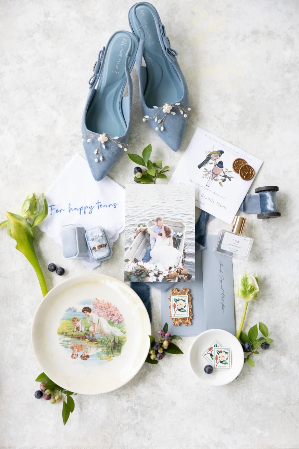 Blue bridal shoes, an antique plate and blueberries arranged with the wedding stationery