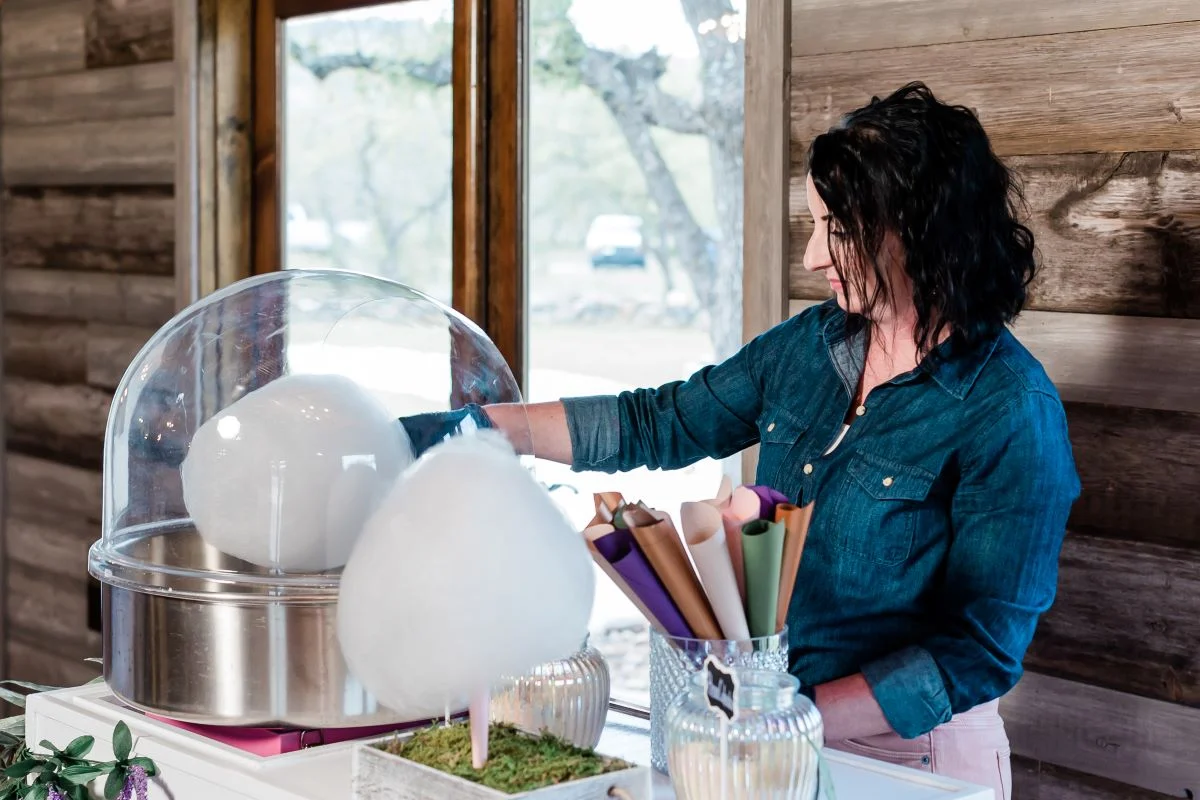 Woman spinning fresh cotton candy at a cart with finished clouds and paper cones nearby