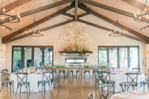The Willow Ridge reception hall with a stone fireplace, wood beam ceiling, round tables and cross-back chairs