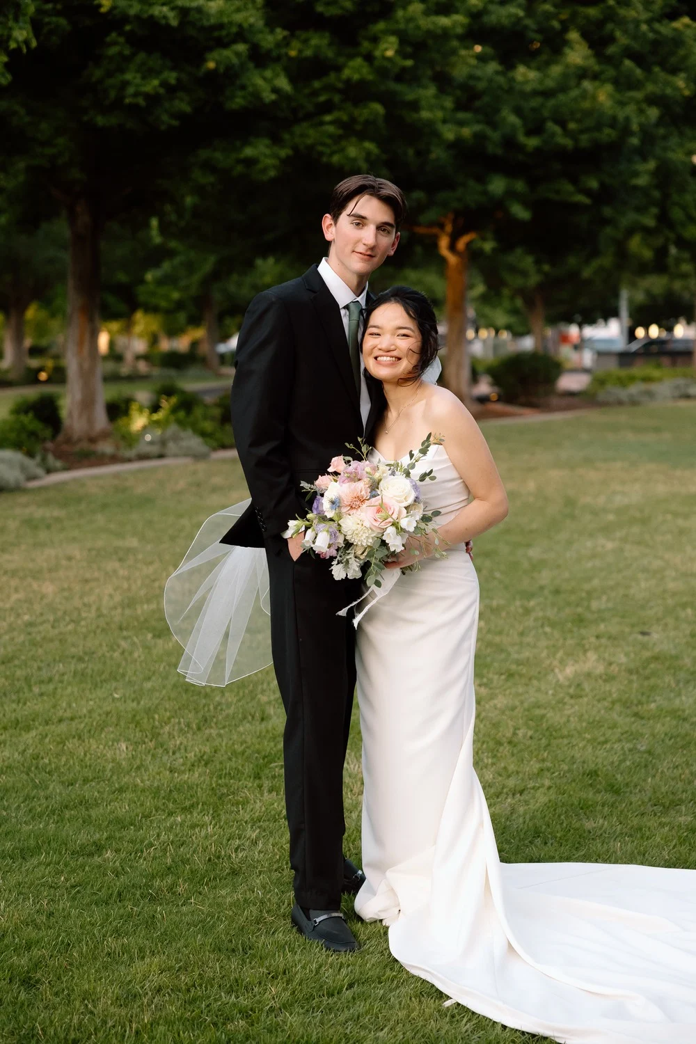 Gabriel and Merribelle on the lawn with her bouquet of pink and white roses and eucalyptus