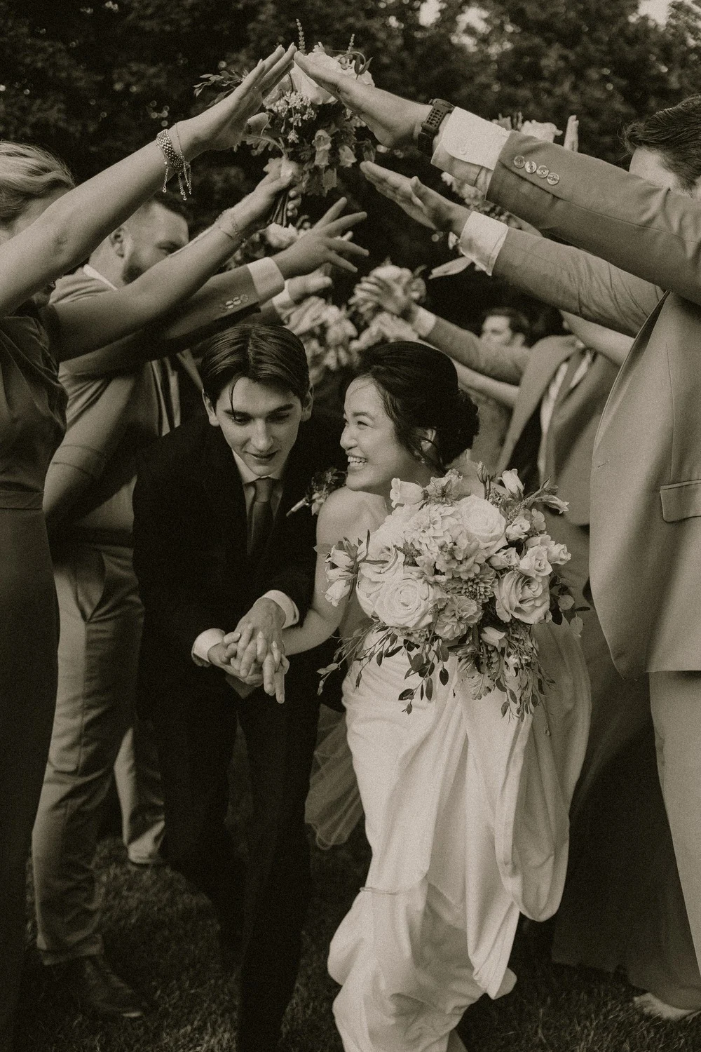 Gabriel and Merribelle Dennis walk beneath an arch of bouquets held by their wedding party