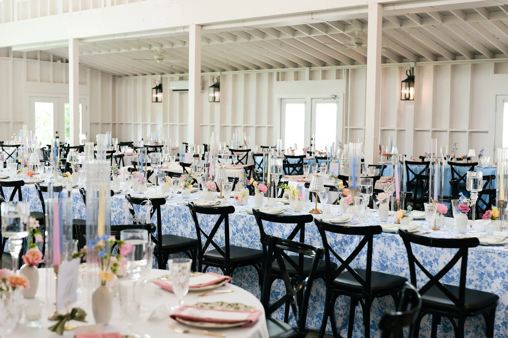 Reception hall at Posey Meadows set with blue and white floral linens and black cross-back chairs