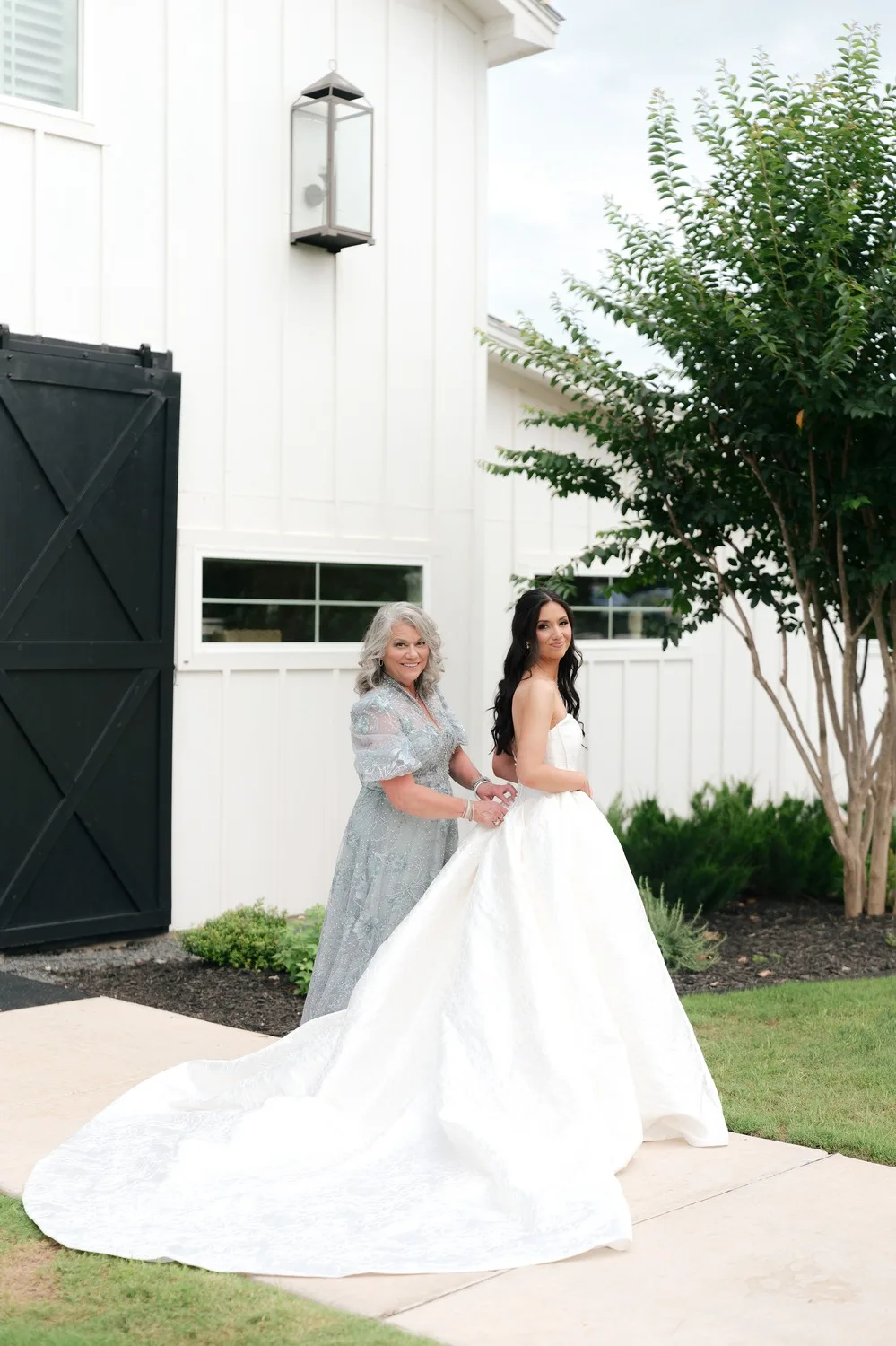 A woman in a silver gown helps with the train of Rebecca's ivory strapless ballgown