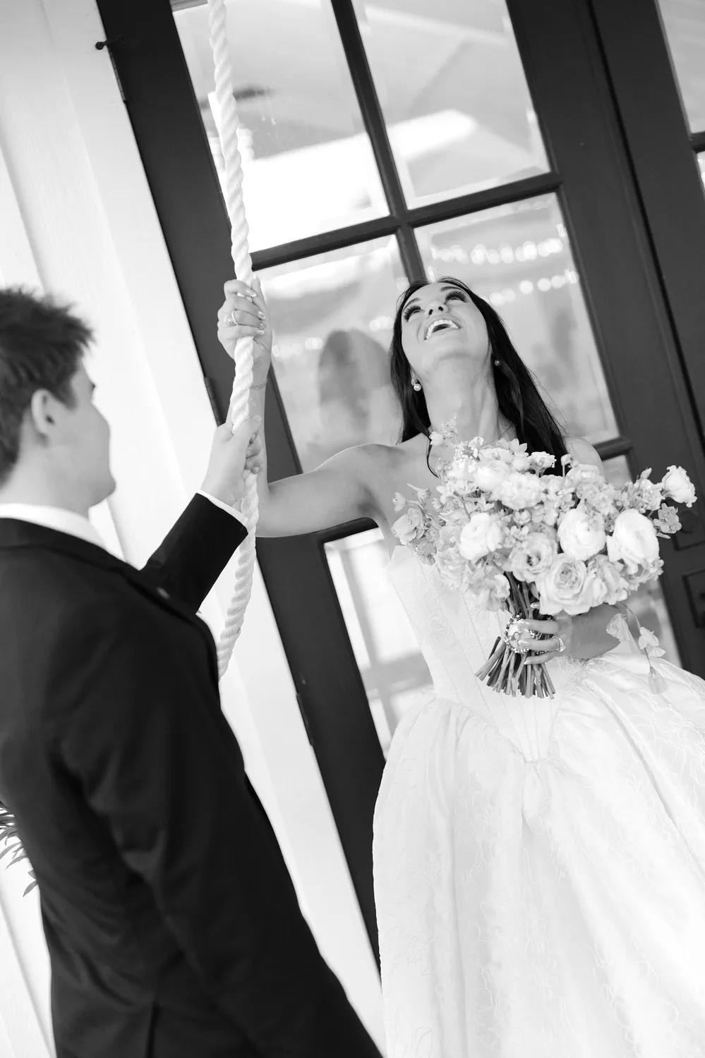 Black and white photo of Rebecca laughing as she and Parker pull the rope of the chapel bell