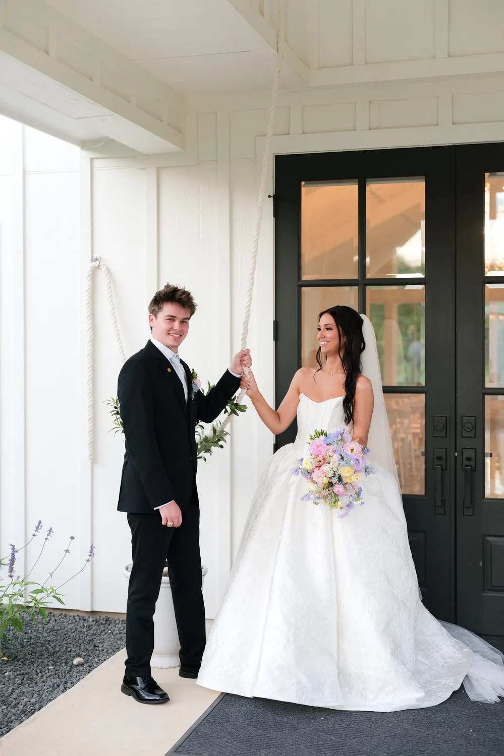 The couple rings the chapel bell outside its black double doors, her bouquet in hand