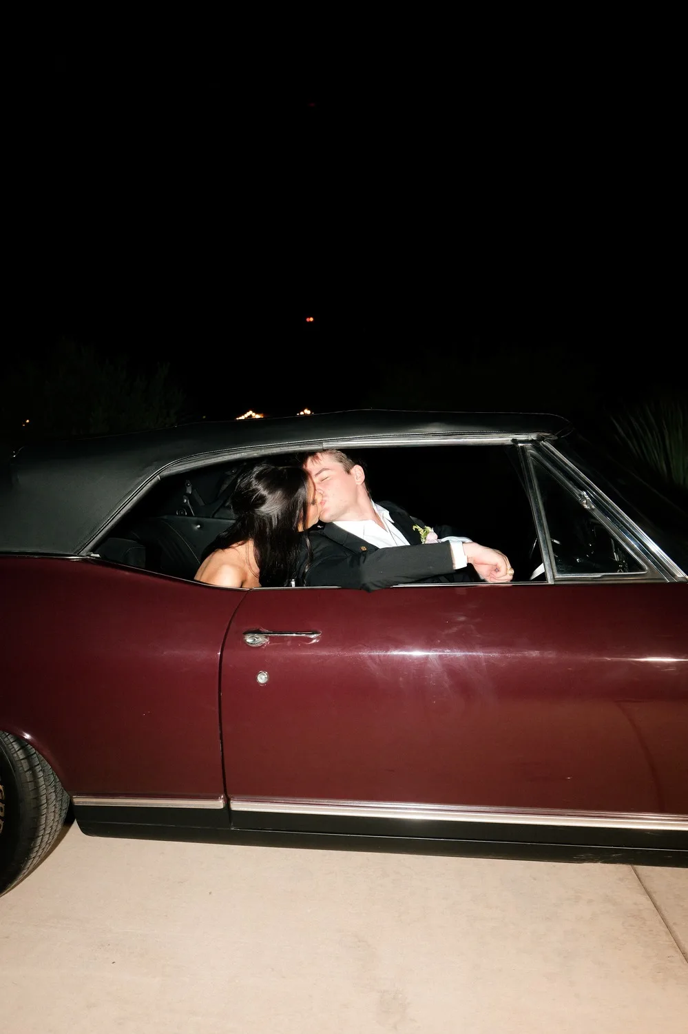 The couple shares a kiss in the vintage convertible getaway car at night