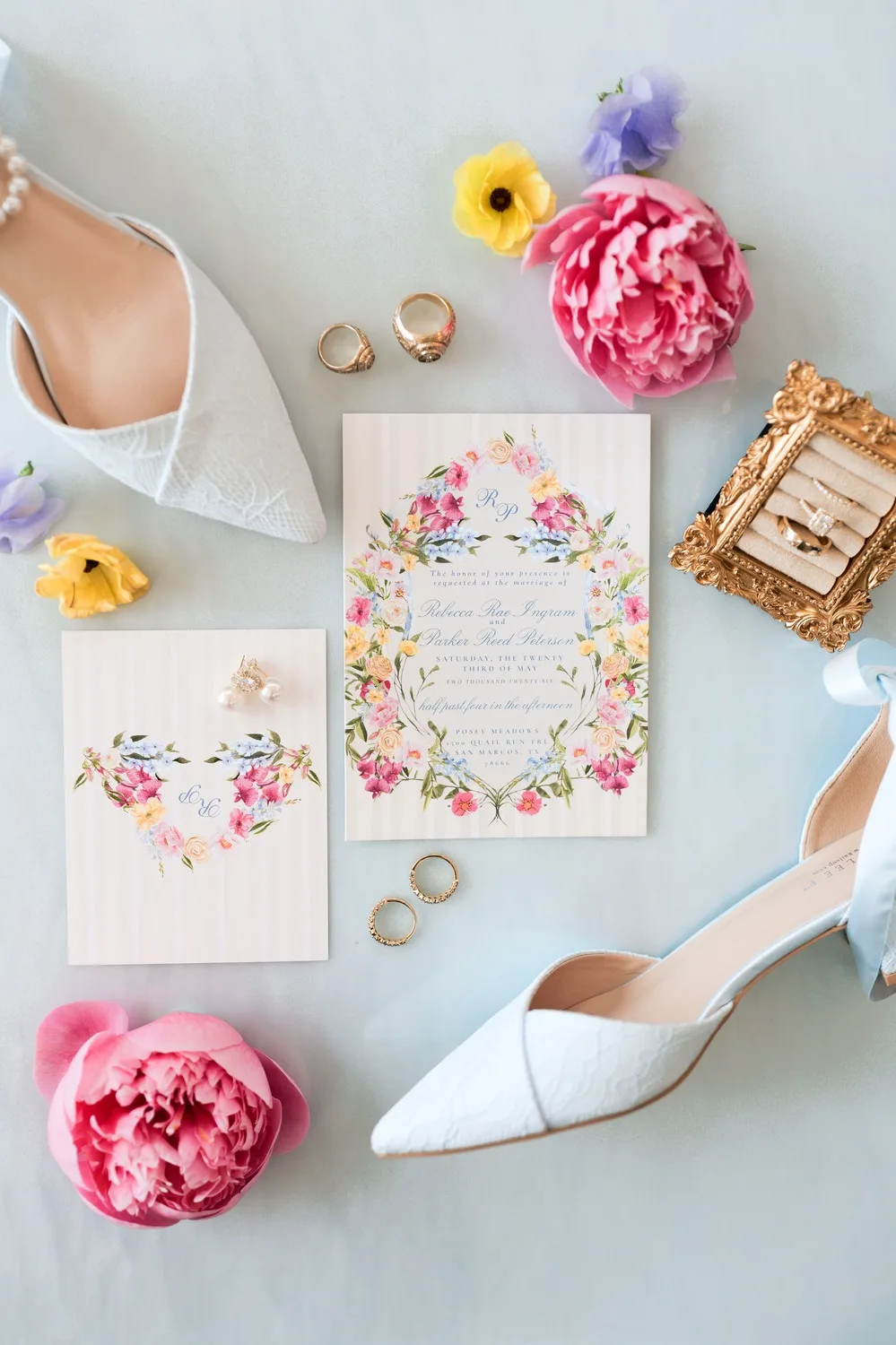 Flat lay of Rebecca and Parker's watercolor floral wedding invitation with rings, bridal heels and peonies