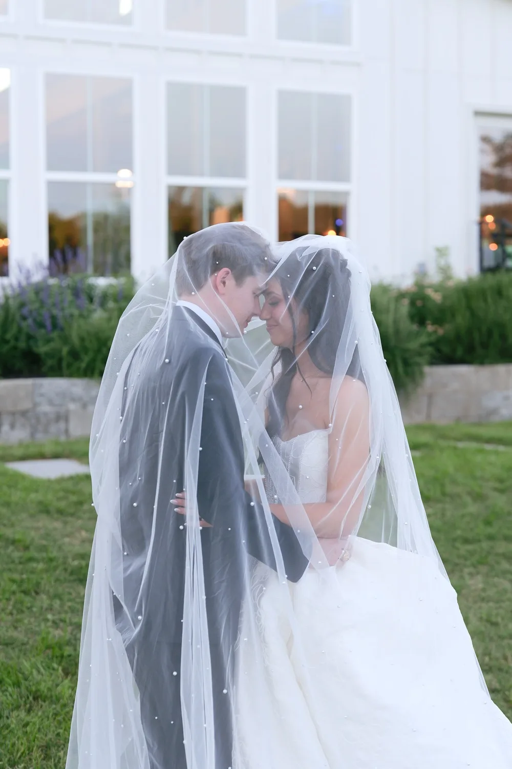 The couple shares a quiet moment beneath the bride's long pearl-dotted veil