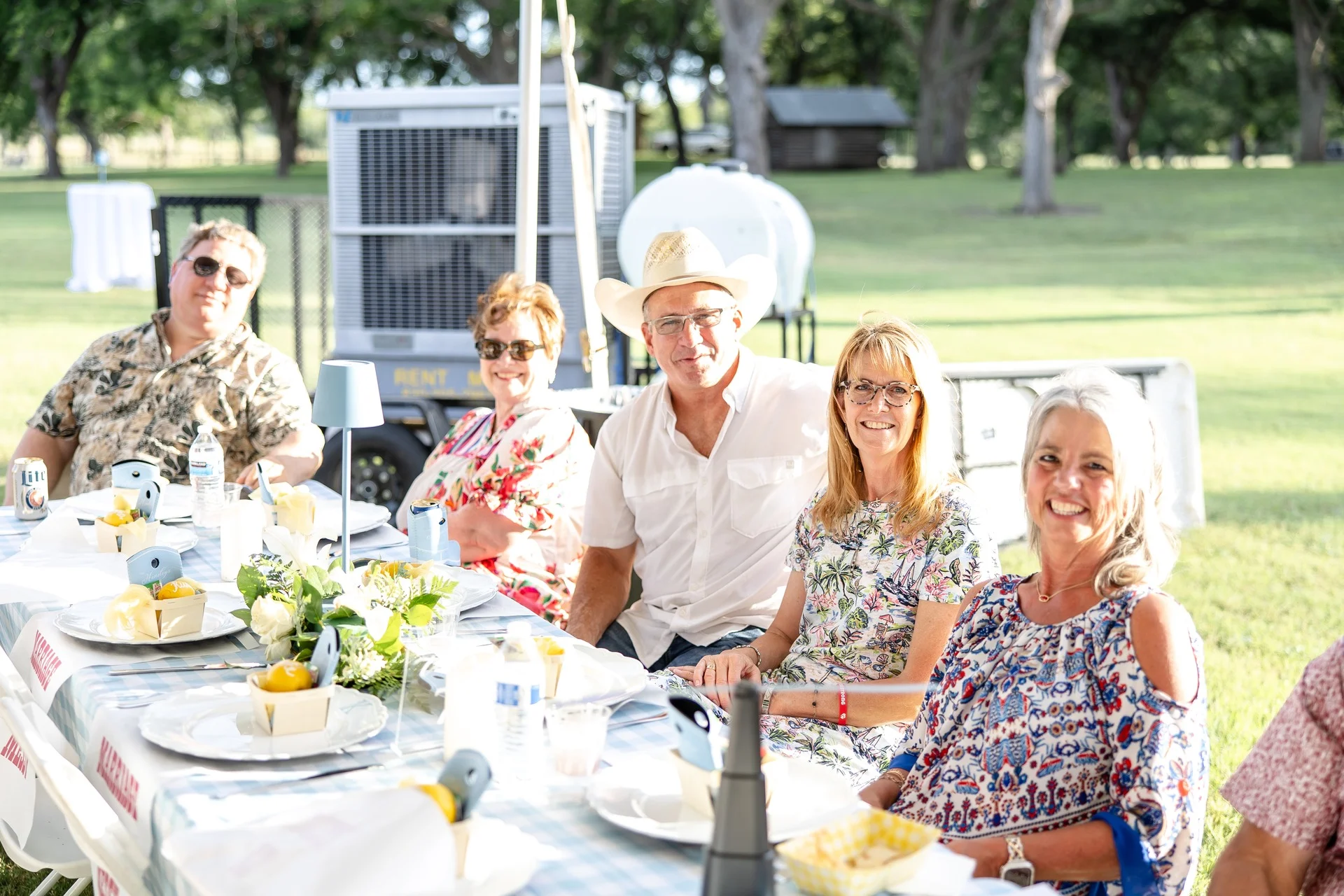 Guests at a gingham-draped reception table under the ranch oaks