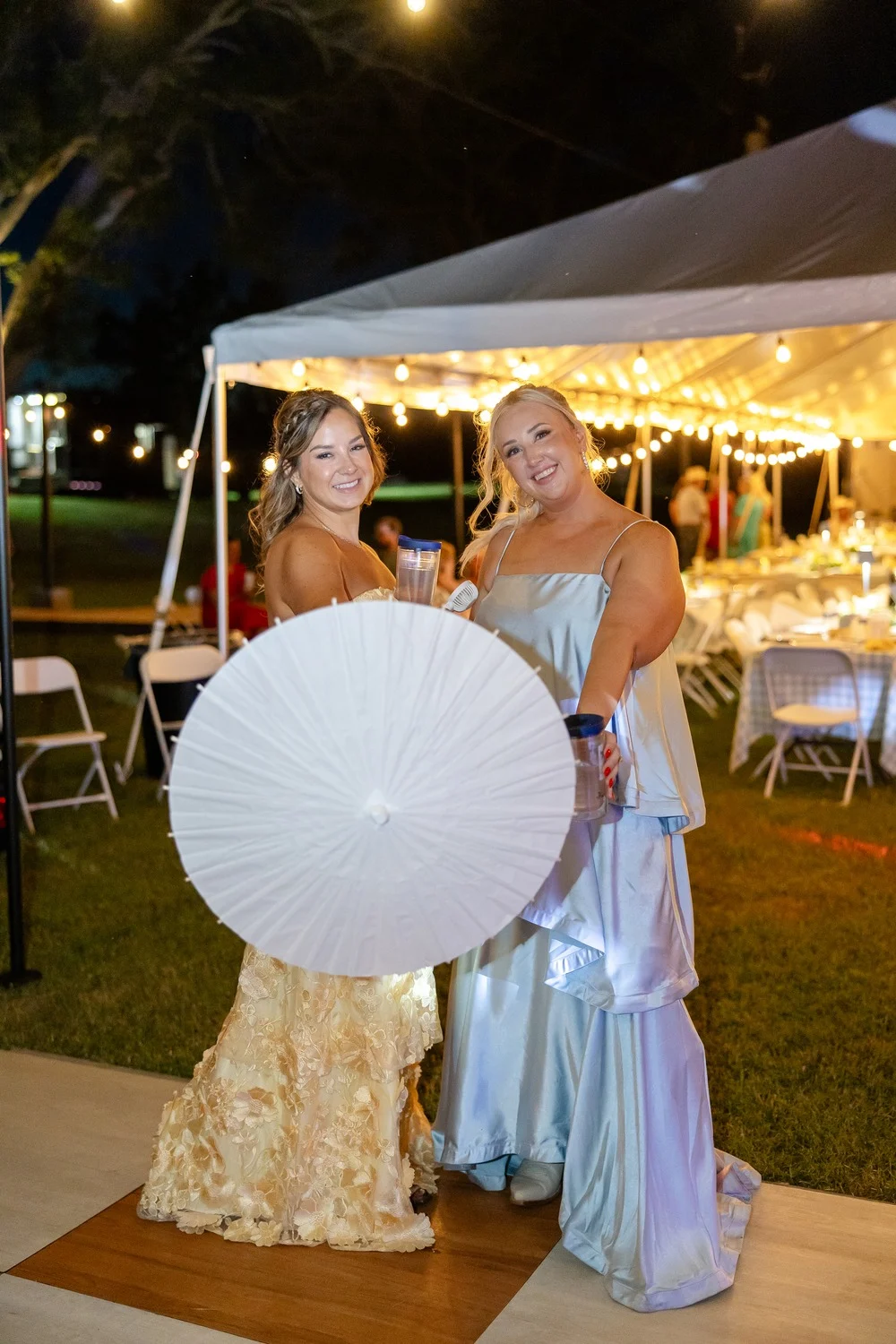 Guests with a white parasol outside the lit reception tent after dark